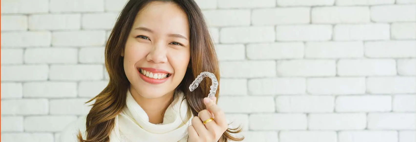 woman holding up an Invsialign clear aligner