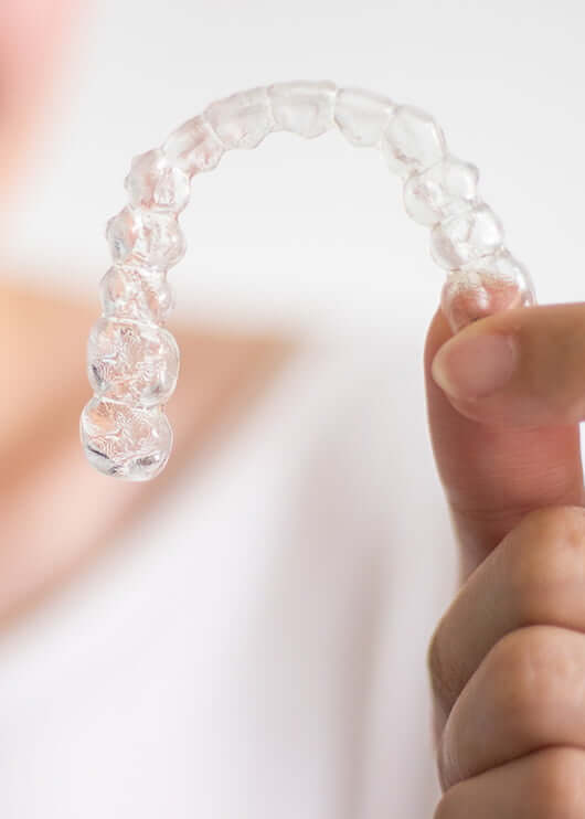 closeup of a person holding up an Invisalign clear aligner