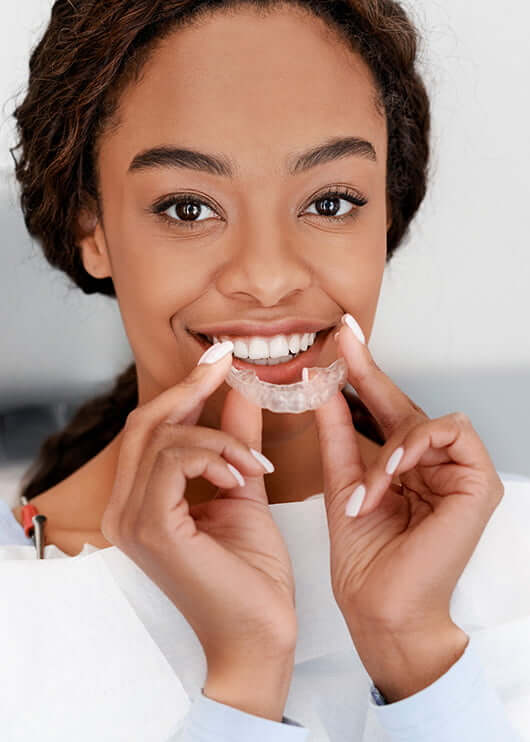 woman inserting a clear aligner onto her teeth